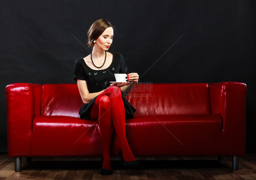 时装和放松概念妇女全长的倒退式高雅女士在室内红沙发上坐着喝咖啡茶杯热饮料图片
