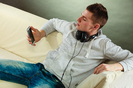 年轻英俊男子在家用耳机智能手在沙发上放松图片