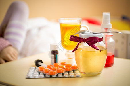 茶蜂蜜罐子和药片放在卧室桌上的图片