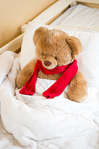 穿着红围巾的棕色泰迪熊躺在毯子下的床上图片