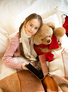 可爱女孩的肖像读书给床上的泰迪熊看书图片