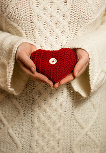 穿着毛衣的红编织心脏的女人照片图片