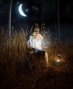 美丽的女人坐在夜间森林读童话故事书的神奇照片图片