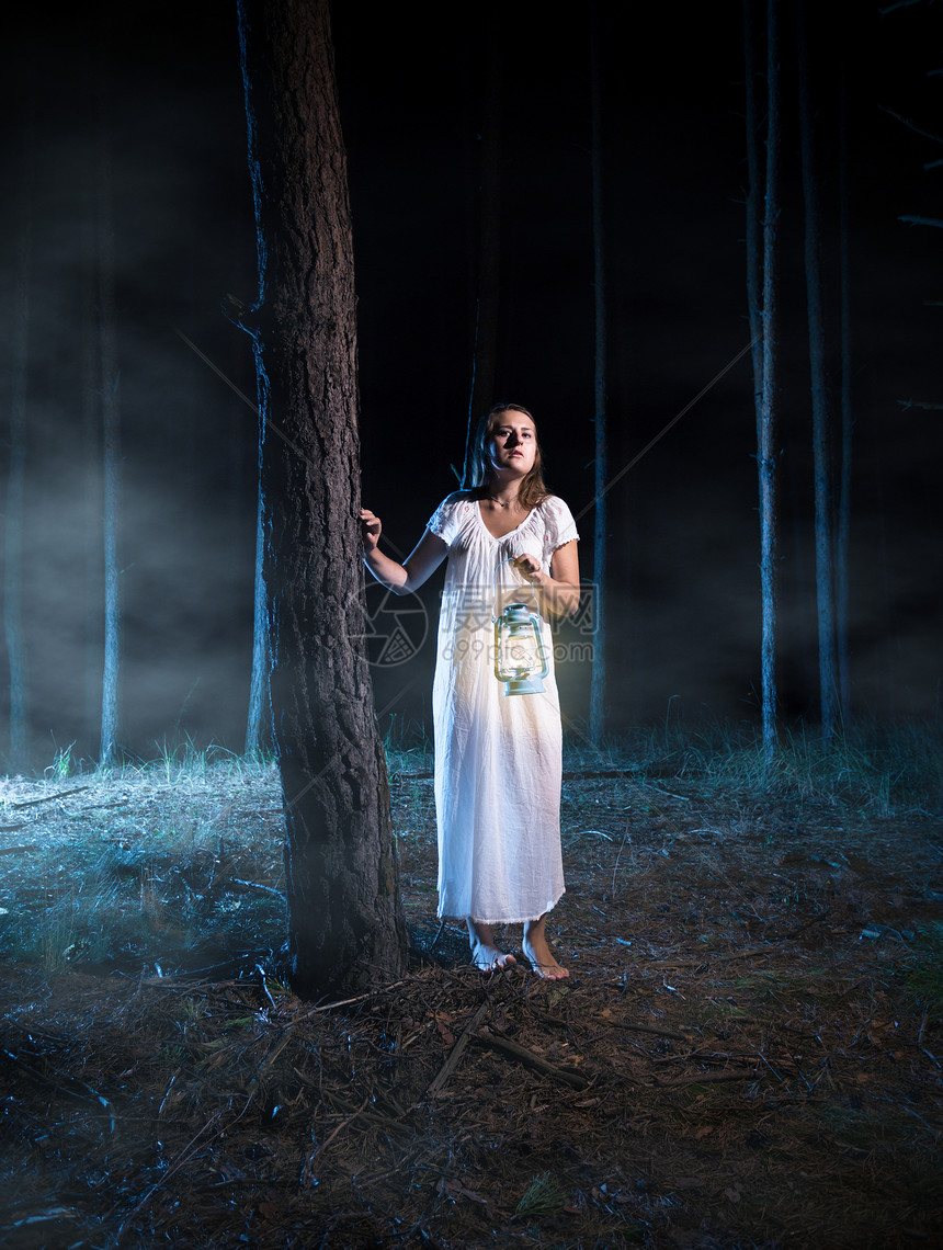 害怕的年轻女青在雾的夜间森林中走着灯笼图片
