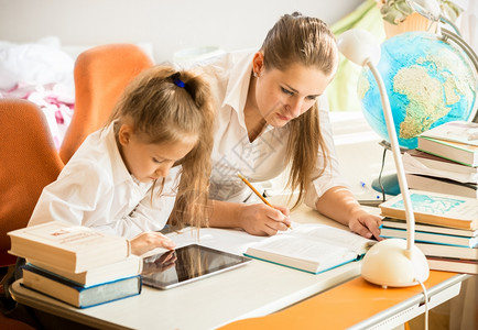 小女孩在母亲做家庭作业而不是做家庭作业时使用数字平板电脑图片