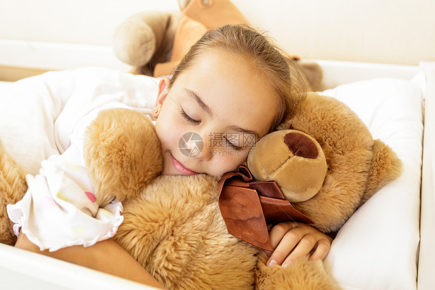 小女孩和大棕色泰迪熊躺在床上图片