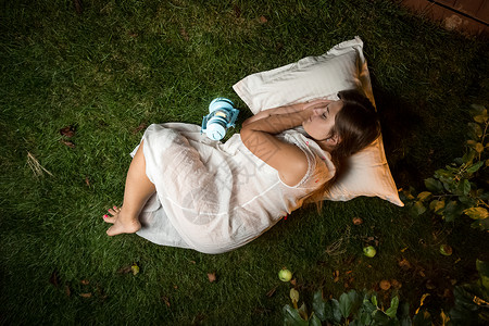 美丽的黑发女睡在枕头的夜间花园图片