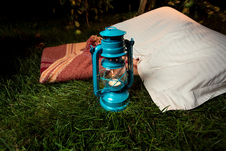 蓝色灯笼素材在枕头和毯子旁边草地上站立的旧油灯贴近镜头背景