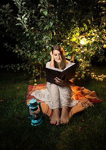 下击暴流妇女晚上在花园灯光下阅读书时挨门外击背景