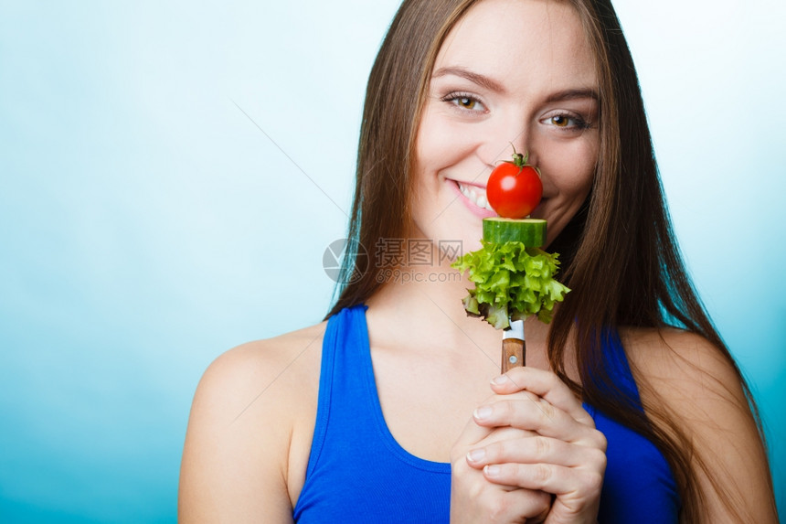 美食和减肥概念有趣的女孩健身人拿着叉子和新鲜混合蔬菜蓝色背景图片