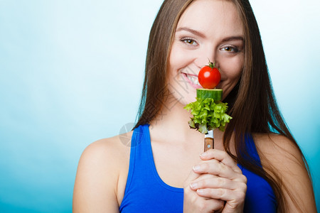 美食和减肥概念有趣的女孩健身人拿着叉子和新鲜混合蔬菜蓝色背景图片