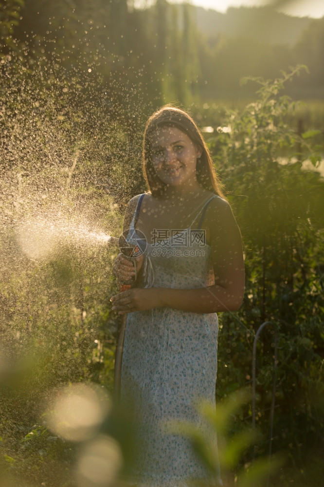 微笑的年轻女子用自来水管在花园里浇的肖像图片