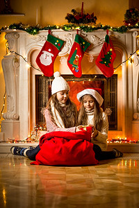 坐在壁炉旁边的漂亮女孩看着Santa礼物背景图片
