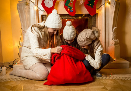 年轻母亲有两个女儿在Santa红色袋内看着两个女儿图片