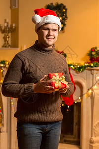 穿着圣诞老人红帽子拿着礼盒在家里装着红礼盒的笑脸男人肖像图片
