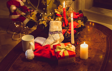 圣诞节蜡烛露天礼品箱和羊绒袜子放在壁炉木桌上背景图片
