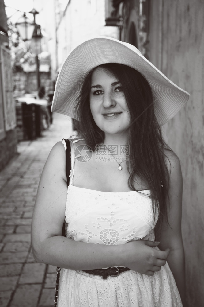 黑色和白的特贴照片身戴帽子的笑着女人在狭窄的街道上行走图片