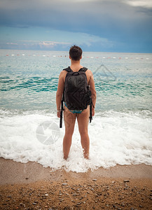身着旅游背包的年轻人站在海边看地平线图片
