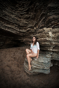 美丽的瘦女人坐在海洞的悬崖上图片