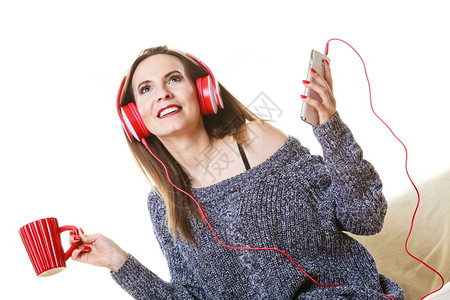 妇女随便的红色大耳机听音乐mp3坐在沙发上家休息喝热茶背景图片