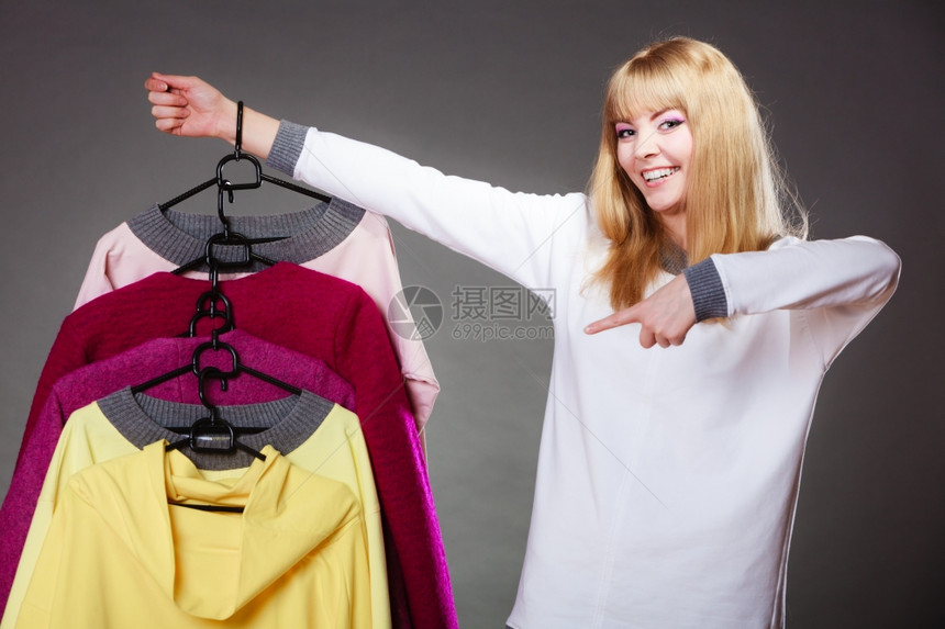零售和销金发美女时装服顾客与衣着多彩灰色背景的手指衣架对着顾客图片