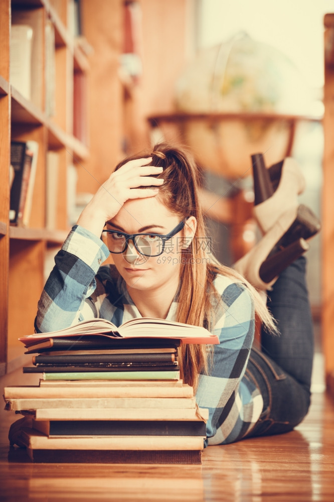 在学校教育概念中身戴眼镜的聪明女学生孩躺在大图书馆的地板上阅读书本图片