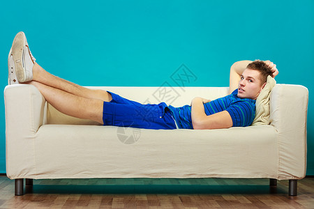 年轻人在沙发上放松少年童睡懒躺在床上蓝背景图片