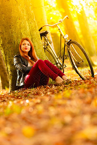 美丽的红发女郎在公园树下挨着自行车席地休息图片