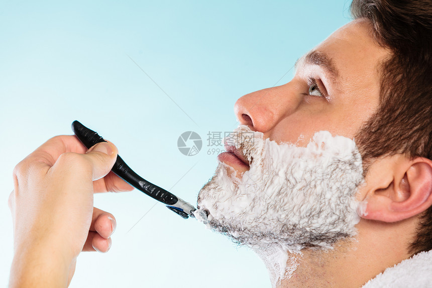 健康美貌和皮肤护理概念关闭年轻胡子男脸部涂着泡沫剃须刀脸部涂着蓝色背景图片
