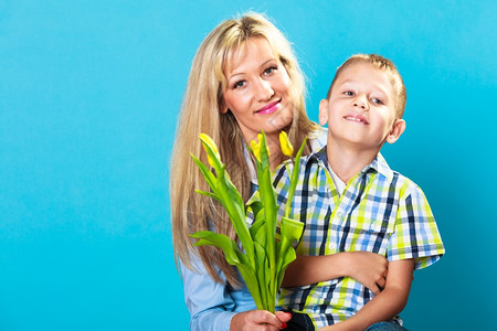 男孩庆祝母亲39日男孩庆祝母亲39日小孩子男给妈工作室送黄色的郁金香花给妈拍蓝色背景图片