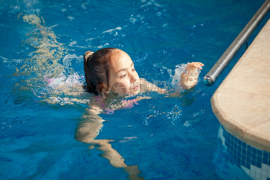 年轻女孩游泳到池边缘图片