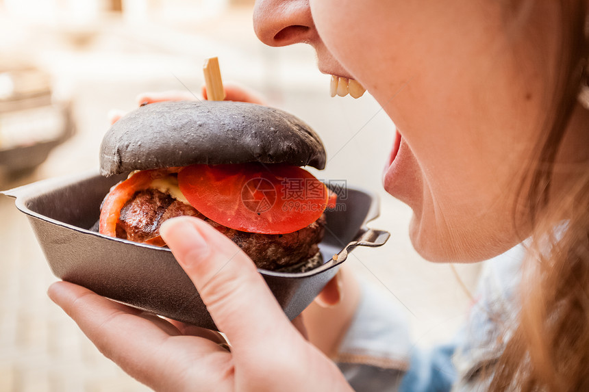 女人用大理石牛肉咬黑汉堡的肖像图片