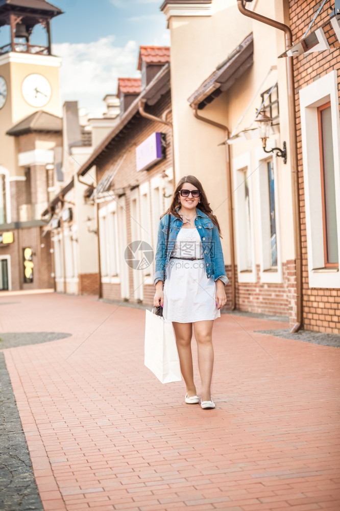 快乐的笑女人白色购物袋在老街上行走图片