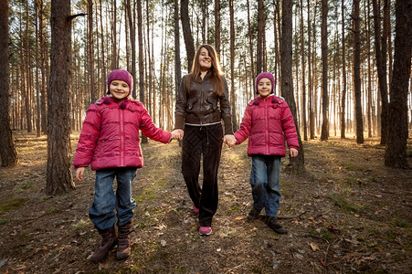 美丽的母亲和两个女儿在阳光明媚的森林中行走图片