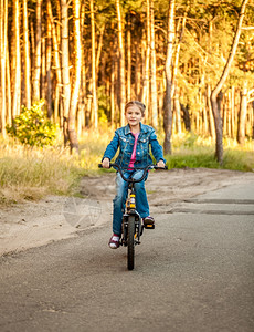 可爱的小女孩在森林路上骑自行车图片
