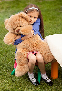 沮丧的小女孩抱大泰迪熊坐在院子里的椅上图片