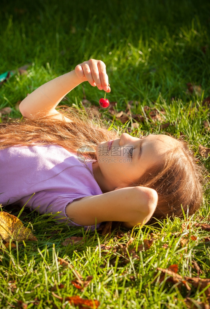 小女孩躺在草地上看着红樱桃图片