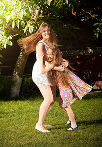 美丽的年轻母亲和女儿在院子里的草地上跳舞图片