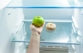 女手握苹果而不是冰箱中甜圈的近照图片