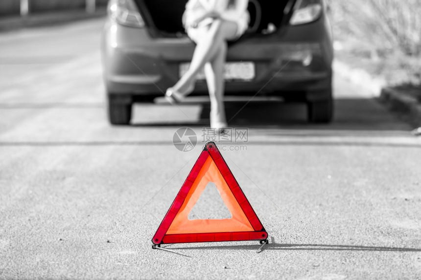 在红色警告标志下妇女坐在破碎的汽车上图片