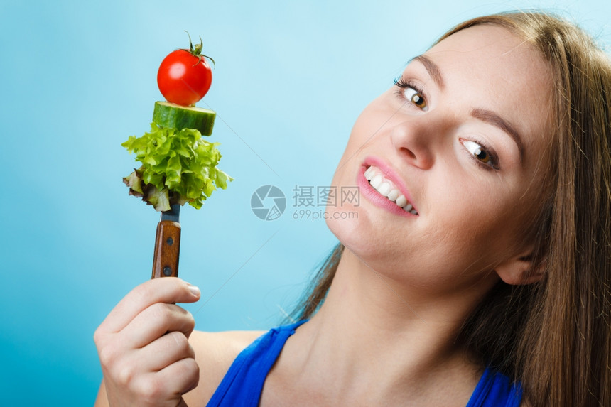 健康的饮食和概念快乐的年轻女子拿着蓝底蔬菜工作室拍摄图片