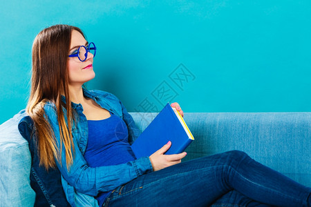 休闲教育文学和家庭概念戴眼镜蓝色牛仔裤眼镜的妇女坐在家沙发上阅读书图片
