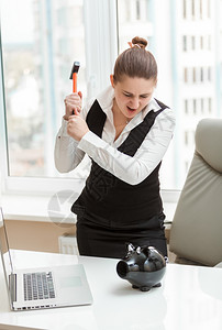 办公室的愤怒女人用锤子打猪银行的肖像图片