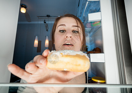妇女从冰箱拿甜圈的宽角肖像图片