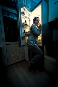 饥饿妇女晚上在冰箱附近吃饭的照片图片