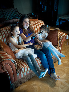 晚上在沙发看电视的母亲和两个女儿的肖像图片