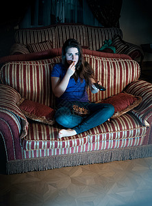 美丽的黑发女晚上在沙发看电视吃爆米花图片