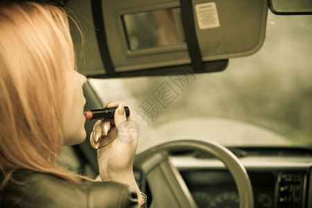 年轻女司机红发少在驾驶汽车时涂唇膏补妆图片
