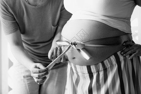 年轻男子在妻和怀孕腹部脱丝带的照片图片