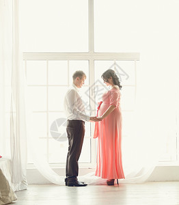 美的怀孕夫妇在大窗口握手的照片图片